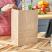 A woman holding a ChoiceHD brown paper bag filled with groceries.