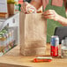 A woman holding a Choice Natural Kraft paper bag filled with food and a drink.