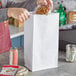 A person putting a plastic container of food into a white paper bag.