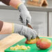 A person wearing Ansell HyFlex cut-resistant gloves cutting a mango on a cutting board.