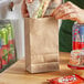 A hand holding a sandwich in a Choice natural Kraft paper bag.