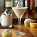 A glass of coffee with Monin cupcake flavoring syrup with cupcakes on a table.