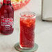 A glass of IBC Black Cherry Soda with ice on a table next to a bottle of IBC Black Cherry Soda.