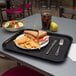 A Carlisle black plastic fast food tray with a sandwich and chips on it.