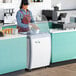 A woman in a blue apron working at a white and grey Avantco gelato dipping cabinet.