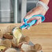 A person using a blue tool to pour liquid into a measuring cup.