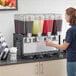 A woman pouring brown liquid into a Carnival King refrigerated beverage dispenser.