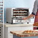 A person putting a baking tray of food into a Cooking Performance Group countertop convection oven.