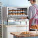 A man wearing an apron puts trays of cupcakes in a Cooking Performance Group countertop convection oven.