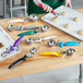 A woman using a white ergonomic thumb press disher to scoop cookie dough into a silver bowl.