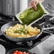 A person pouring Armanino basil pesto into a bowl of pasta.