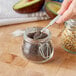 A person holding a spoon over a Choice glass storage jar of seeds.