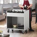 A man in an apron using a ServIt stainless steel flatware cart in a professional kitchen.