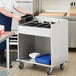 A woman in a school kitchen putting flatware trays into a ServIt stainless steel tray cart.