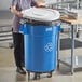 A woman standing next to a Lavex blue round commercial recycling can with a white lid.