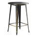 A black metal bar stool with a gold base sitting at a Lancaster Table & Seating distressed gold bar table.