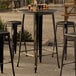 A Lancaster Table & Seating Alloy Series bar table and chair set with a distressed gold table top and black chair legs.