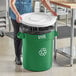 A woman putting a white lid on a green Lavex recycling can.