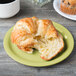 A croissant on a GET Avocado Diamond Harvest melamine plate next to a cup of coffee.