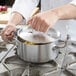 A person using a Vollrath Miramar casserole pan to cook food on a stove.