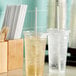 A wooden tray with two clear plastic cups filled with a drink and Aardvark white paper straws in a plastic cup.