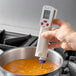 A hand using a Cooper-Atkins digital infrared thermometer to check the temperature of soup.
