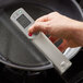 A hand holding a Cooper-Atkins digital thermometer with a screen over a pan.