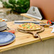 A Chicago Brick Oven pizza on a wooden pizza peel on a table with a Chicago Brick Oven leg stand underneath.