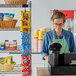 A woman wearing an apron using a Choice hanging chip rack behind a convenience store counter.