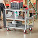 A man standing next to a Lavex steel utility cart with three shelves.