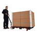A man pushing a Vestil steel wheel nose pallet truck with a large box on it.