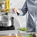 A woman using a Vollrath wire mesh skimmer to cook vegetables in a pot on a stove.