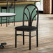 A Lancaster Table & Seating spoke back chair with a black fabric seat sits in front of a table in a restaurant dining area.