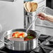 A hand holding a Vollrath Jacob's Pride heavy-duty two-piece skimmer stirring a pot of soup.
