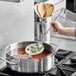 A hand using a Vollrath round skimmer to stir soup in a pot.