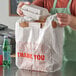 A person putting a styrofoam container into a white "Thank You" plastic bag.