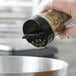 A hand using a black dual flapper spice lid to sprinkle herbs on a salad.