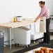 A man wearing an apron standing in a professional kitchen at a Regency wood top work table with a white container on it.