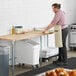 A man in an apron cutting pizza dough on a Regency wood top work table.