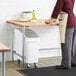 A man in a chef's outfit rolling dough on a Regency wood top work table.