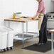 A man in an apron rolling out dough on a Regency wood top work table in a kitchen.