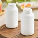Two white 300cc HDPE packer bottles on a wooden surface.