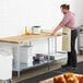 A man wearing an apron stands in a professional kitchen with a Regency wood top work table.