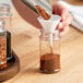 A person pouring a spice into a round plastic jar.