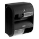 A black Compact by GP Pro Quad Coreless Roll high capacity toilet paper dispenser on a counter with two rolls of toilet paper.