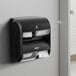 A black and white Compact by GP Pro Quad Coreless Roll high capacity toilet paper dispenser on a wall.