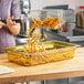A person using a Carlisle amber plastic food pan to fry french fries.