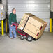 A man pushing a Valley Craft red HVAC hand truck with a large box on it.