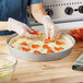 A woman using a Choice aluminum deep dish pizza pan to make a pizza.