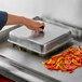 A person using a Choice square aluminum basting cover to hold over a tray of food.